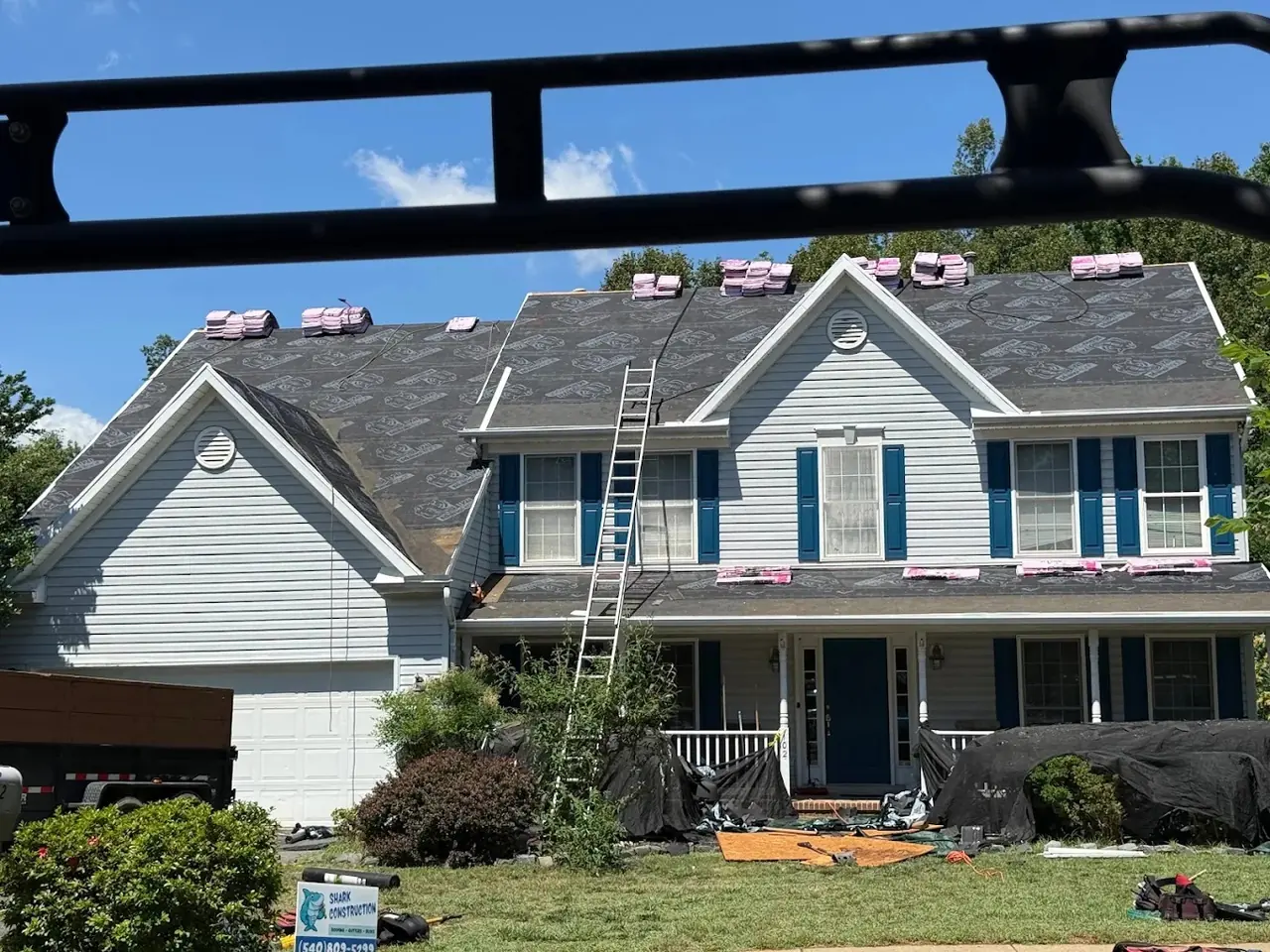 Roof replacement in progress with underlayment, shingle bundles, and Shark Construction yard sign